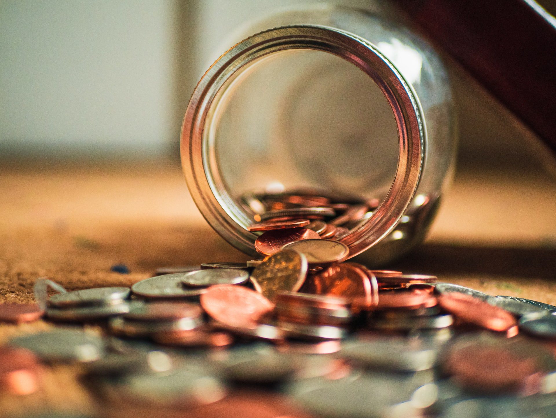 A jar on its side with coins spilling out onto the floor